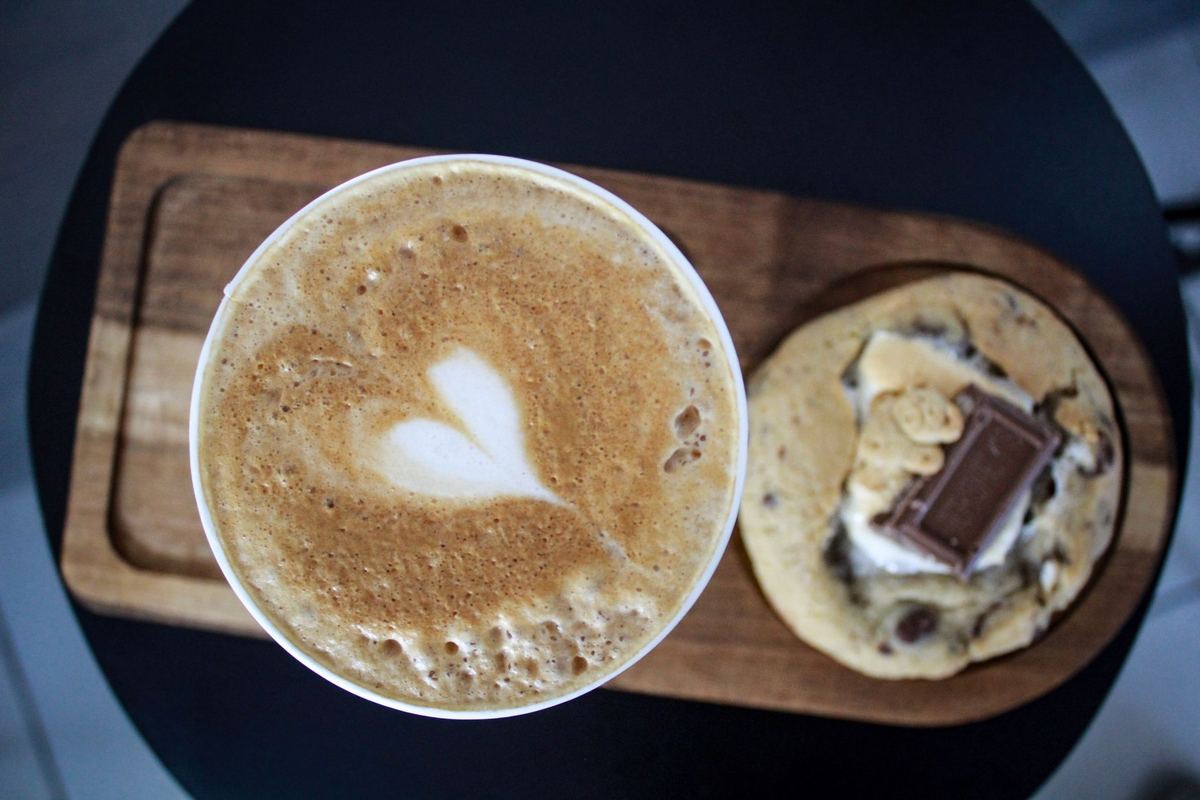 Café con leche y galleta sobre una bandeja de madera